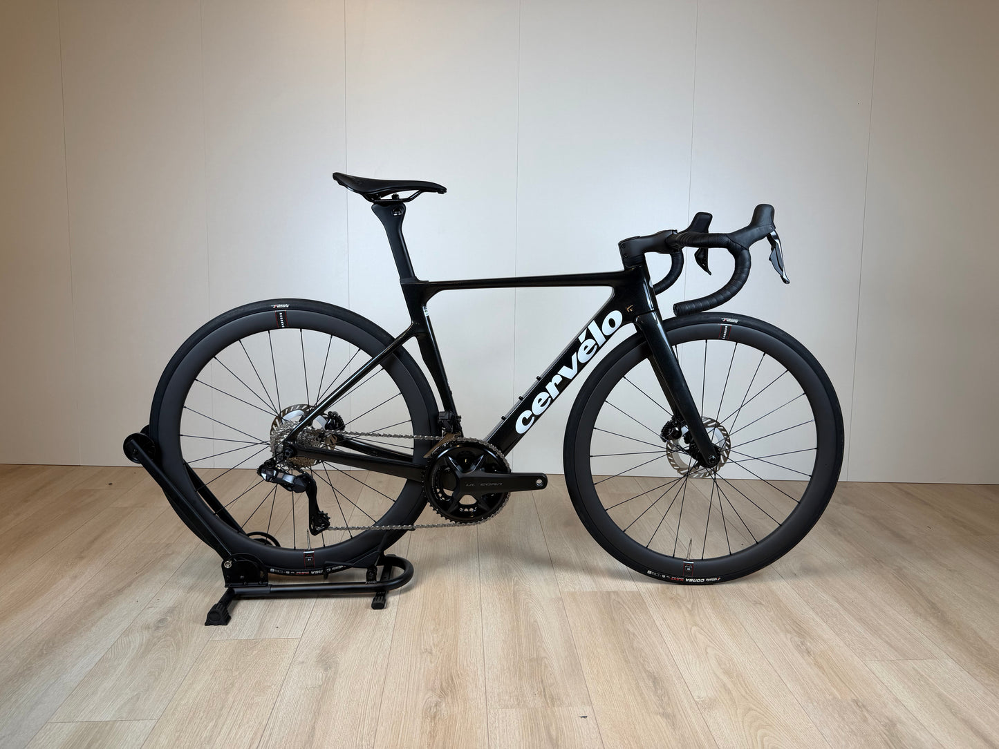 Cervélo Soloist racefiets met zwart frame, aerodynamisch ontwerp, clipless pedalen en dunne banden, op standaard geplaatst.