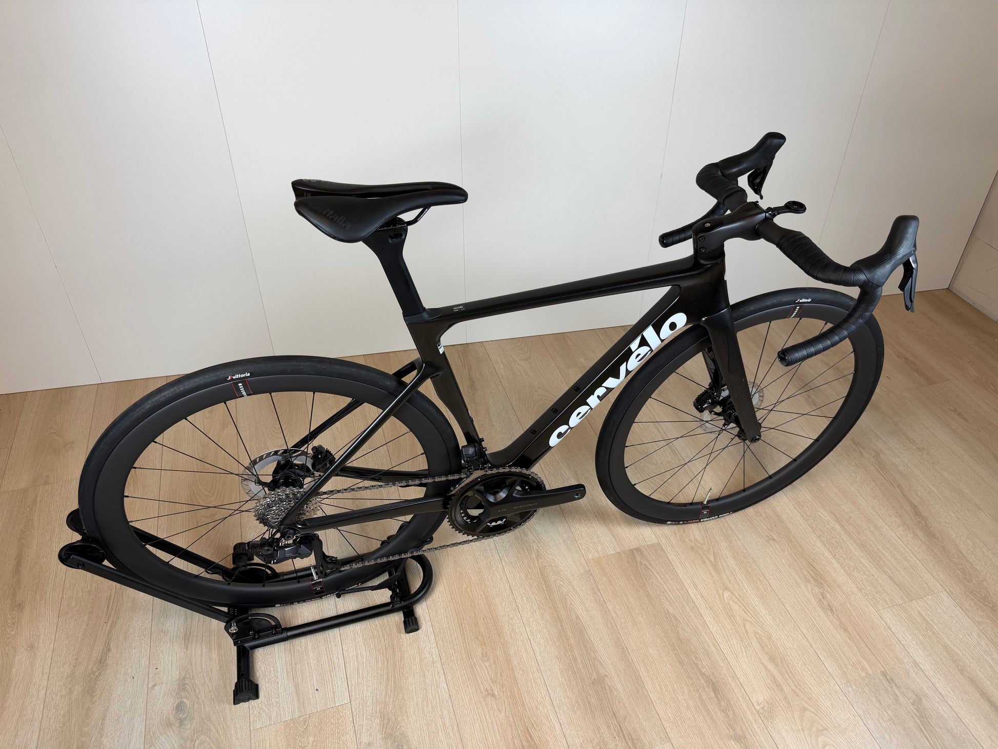 Cervélo Soloist racefiets met zwart frame, dunne banden en aerodynamisch stuur, op houten vloer, door Vélo Studio.