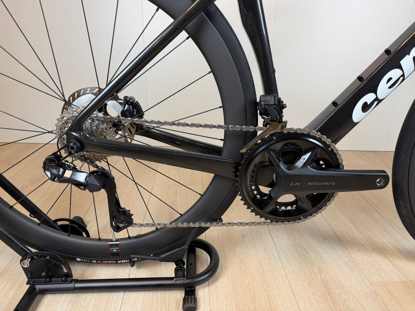 Cervélo Soloist racefiets met zwart frame, ketting en derailleur, close-up van de aandrijving en achterwiel op houten vloer