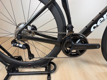 Cervélo Soloist racefiets met zwart frame, ketting en derailleur, close-up van de aandrijving en achterwiel op houten vloer