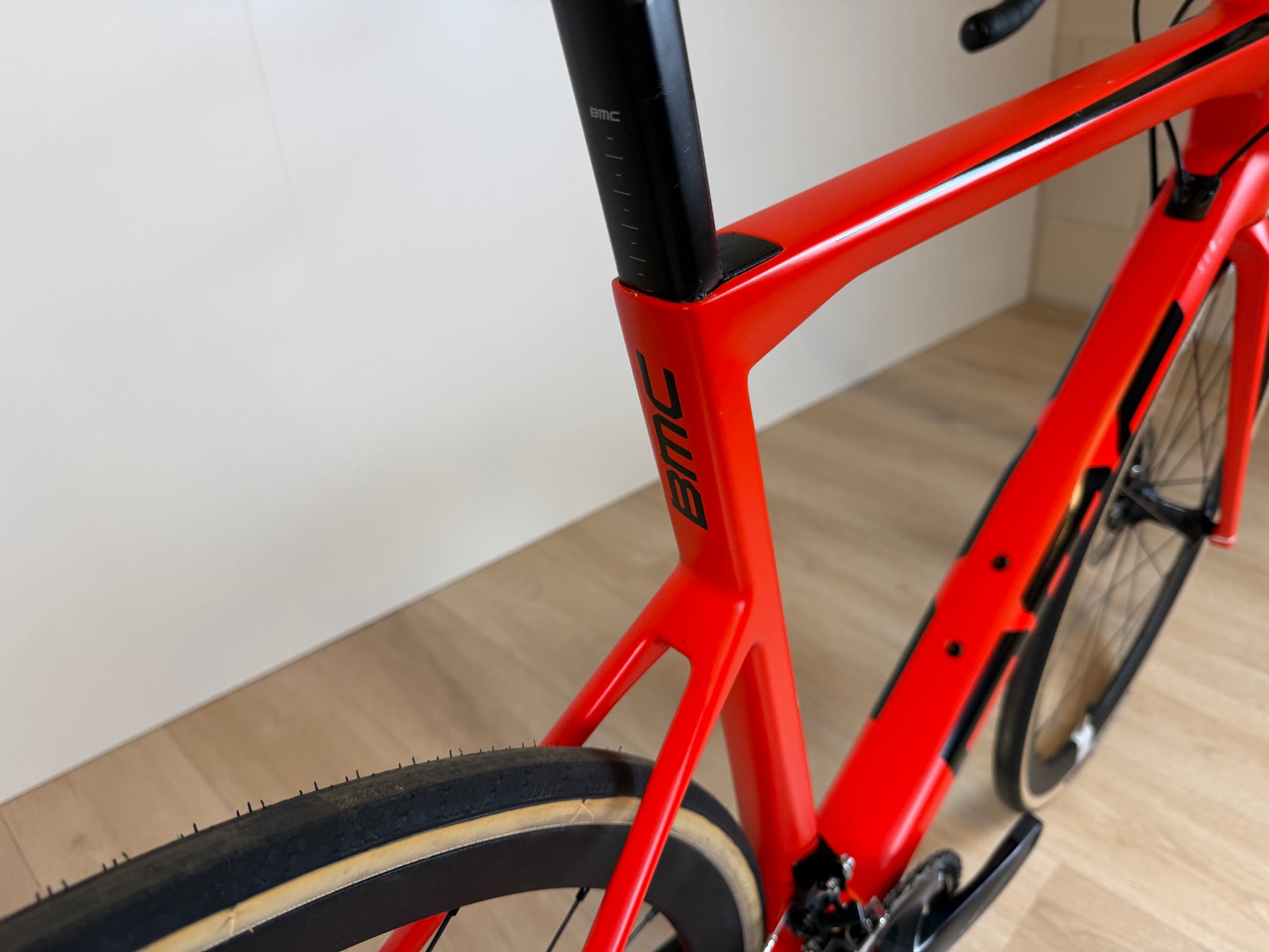 Rode BMC Teammachine SLR FIVE racefiets met aerodynamisch frame en zwart-witte details, gestald op een fietspad.