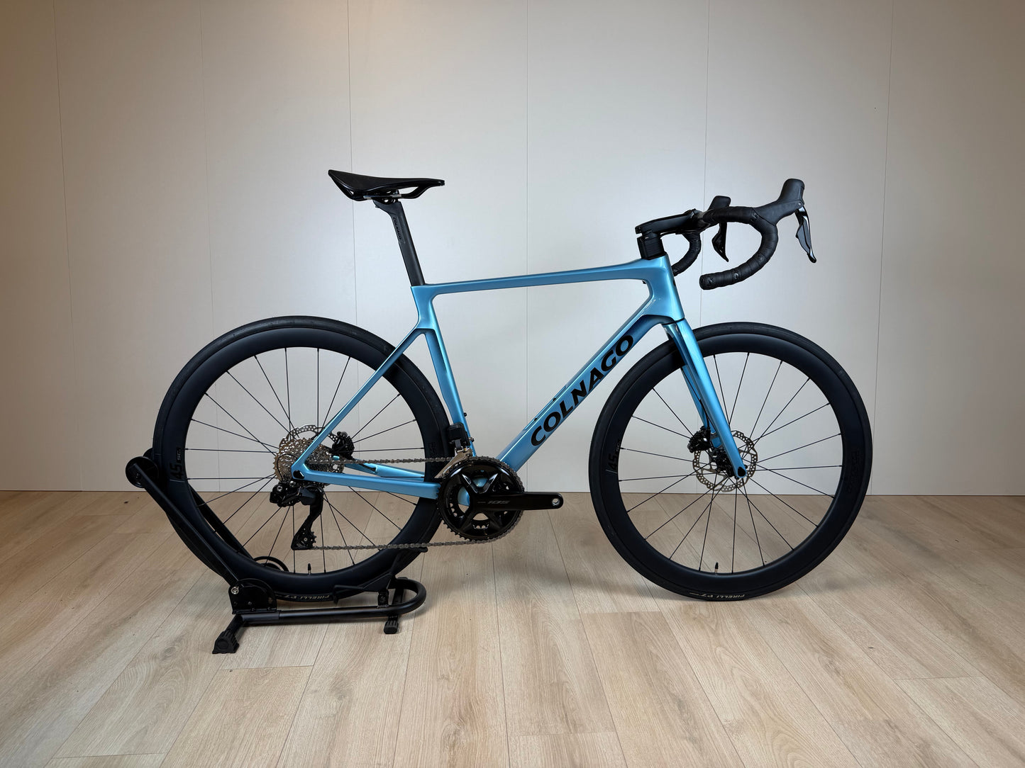 Colnago V4 racefiets met blauwe frame, carbon wielen, drop handlebars en zadel, op een indoor fietstrainer, door Vélo Studio.