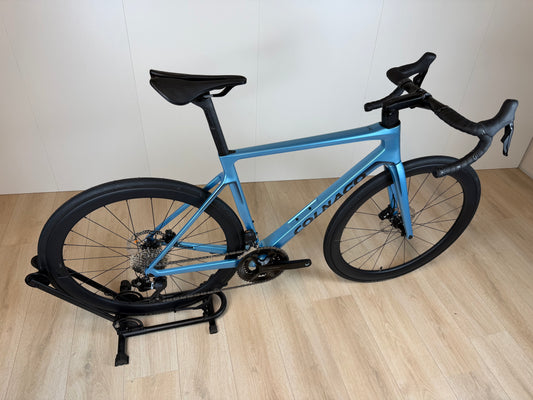 Colnago V4 racefiets met blauwe frame, zwarte wielen en aerodynamisch stuur, geplaatst op houten vloer, door Vélo Studio.