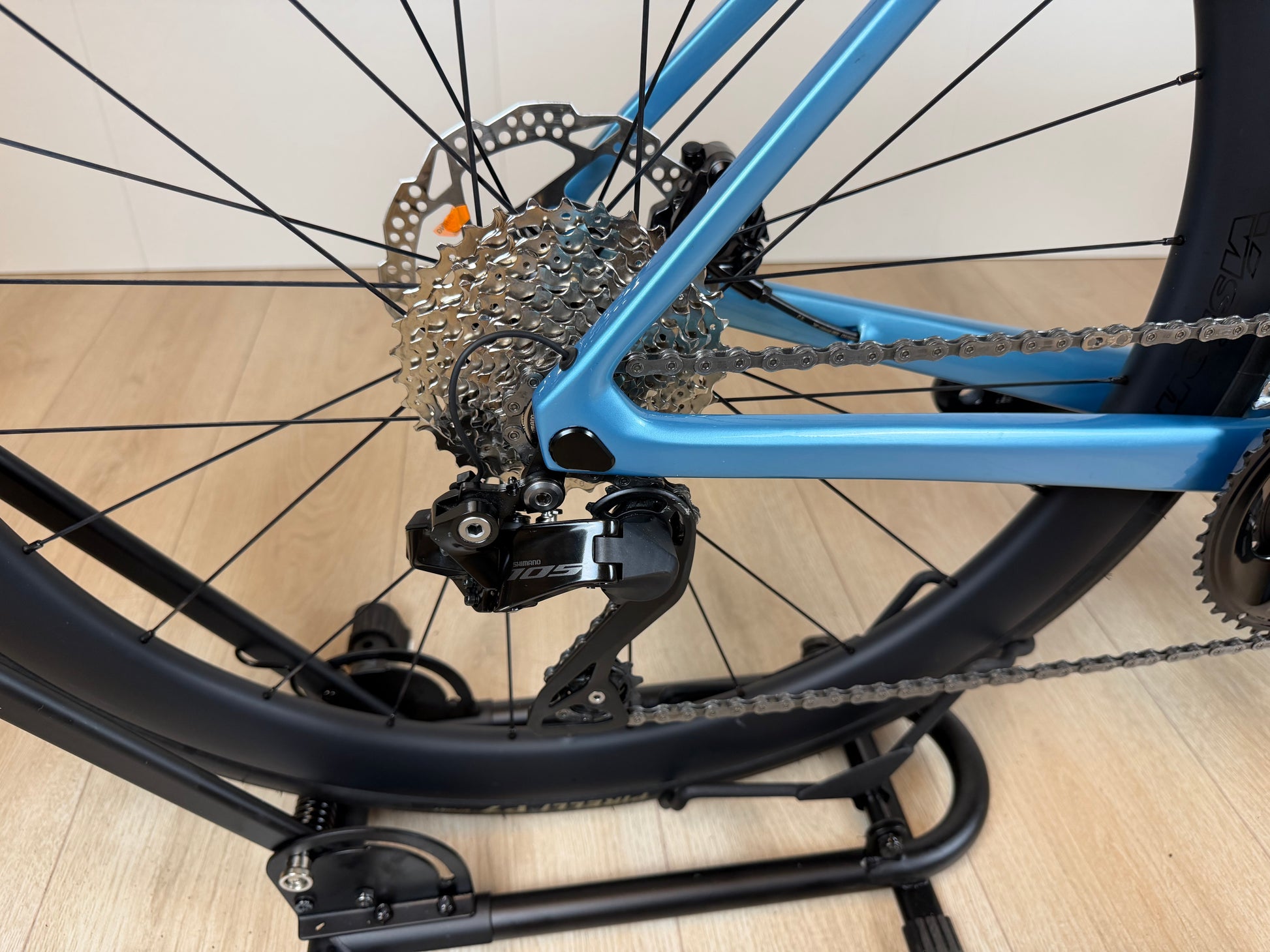 Colnago V4 racefiets frame en achterderailleur, blauw en zwart, met disc remmen en ketting op houten vloer