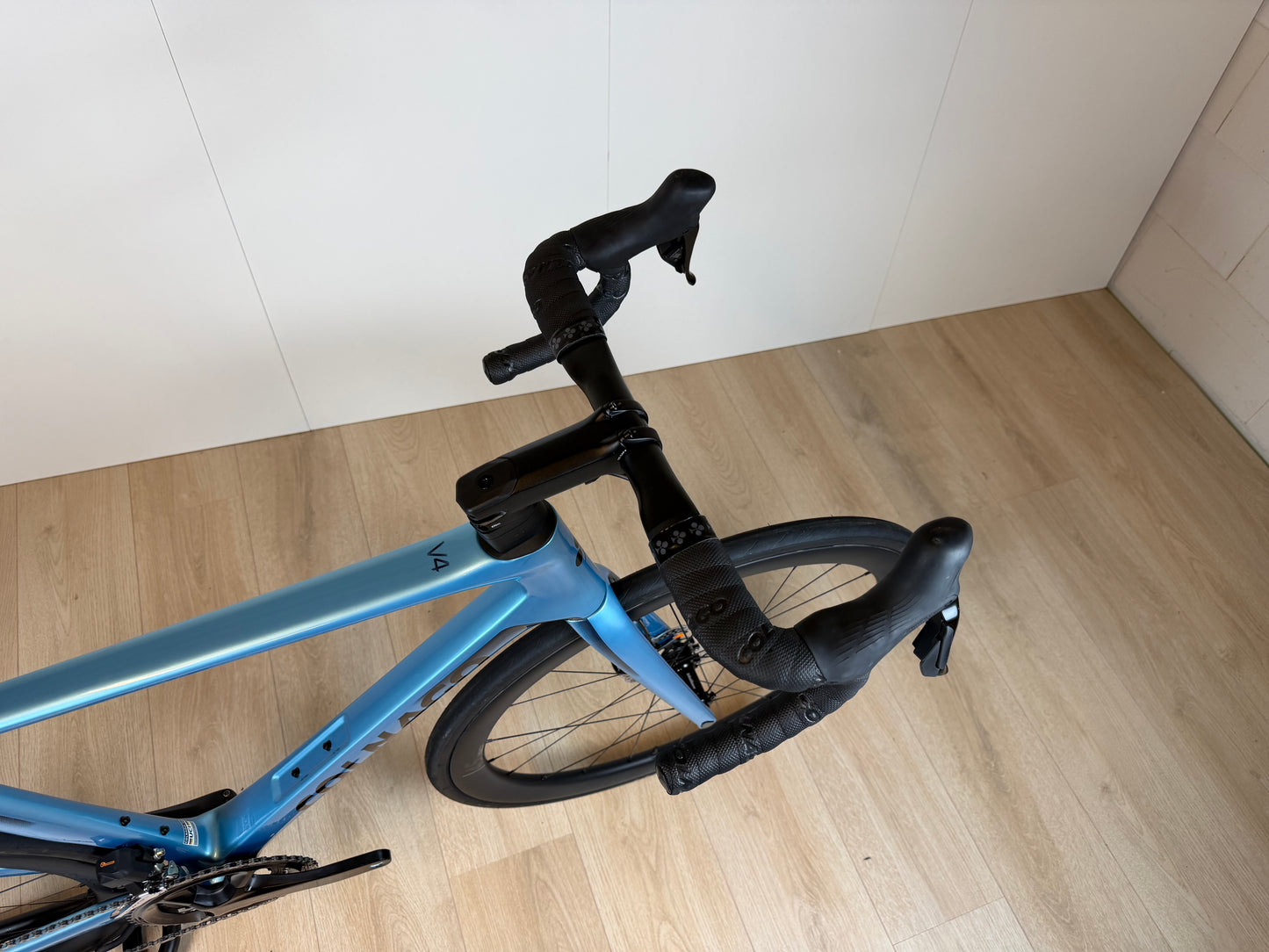 Colnago V4 racefiets met blauwe frame, zwarte stuur en zadel, binnen op houten vloer, door Vélo Studio.