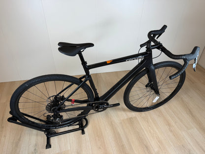 Cervélo Aspero Apex 1 carbon gravelbike, zwart met blauwe accenten, zicht vanaf de zijkant met banden en frame zichtbaar.