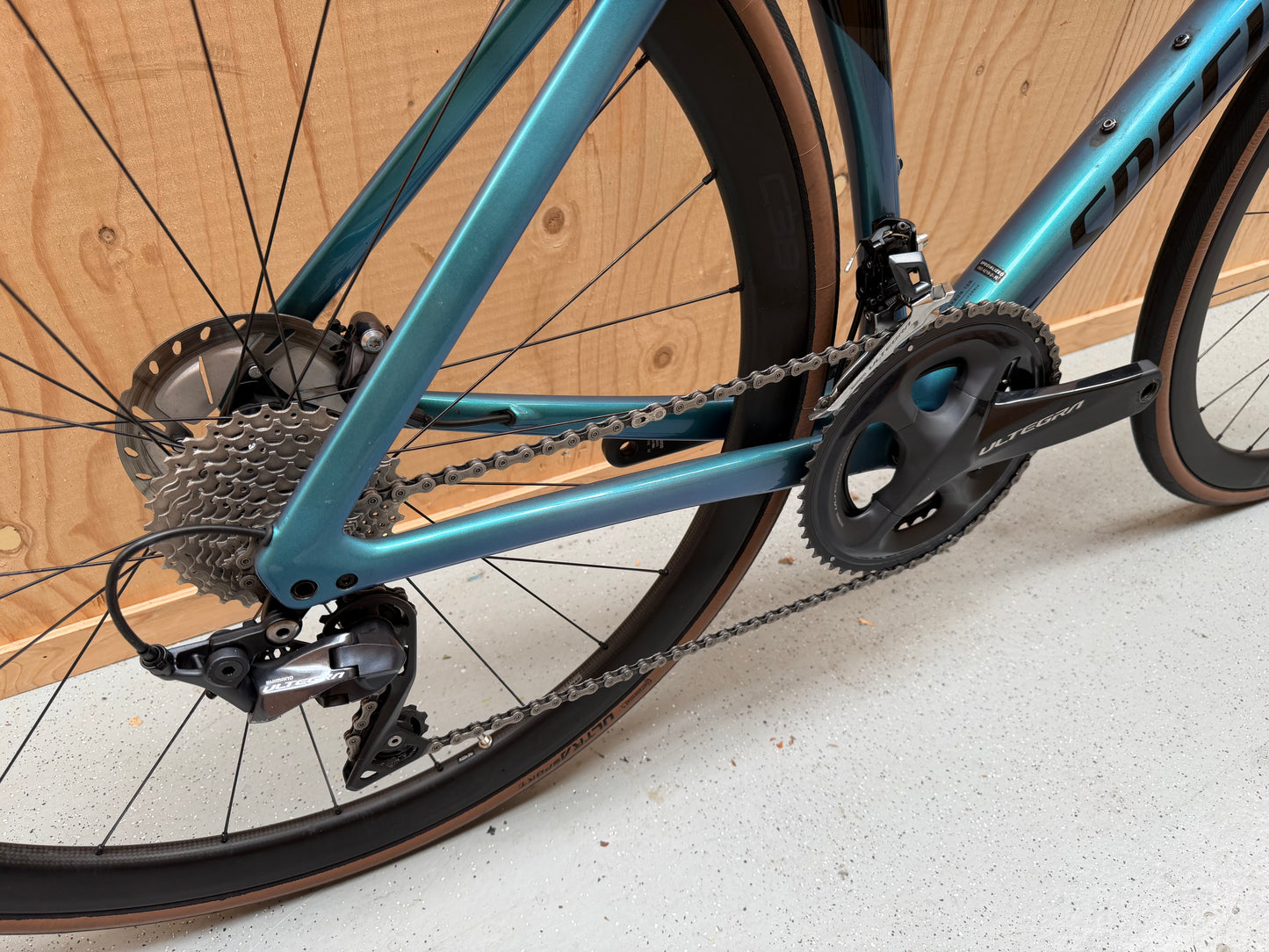 Zwart Specialized Tarmac SL7 Expert racefiets met aerodynamisch frame en dunne banden, naast een fietskader en helm op de achtergrond.