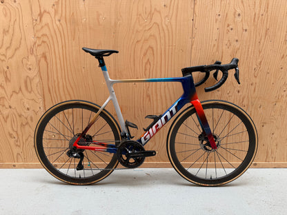 Giant Propel Advanced SL wielrenfiets met Team Jacyo AlUla decals, geparkeerd op een weg, zwart met blauwe accenten.