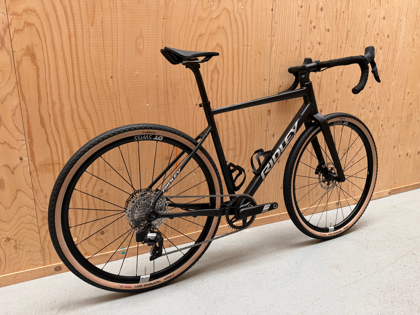 Fietsfoto van de Ridley Adventura mountainbike van Vélo Studio, met zwart frame en off-road banden op gravel ondergrond.