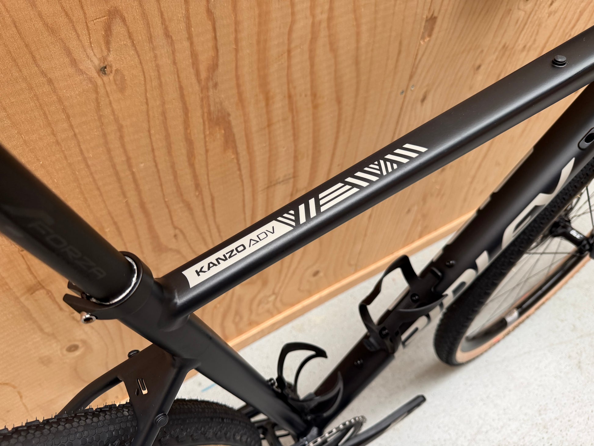 Fietsfoto van de Ridley Adventura mountainbike met zwarte frame en blauwe accenten, liggend op een houten pad in de natuur.
