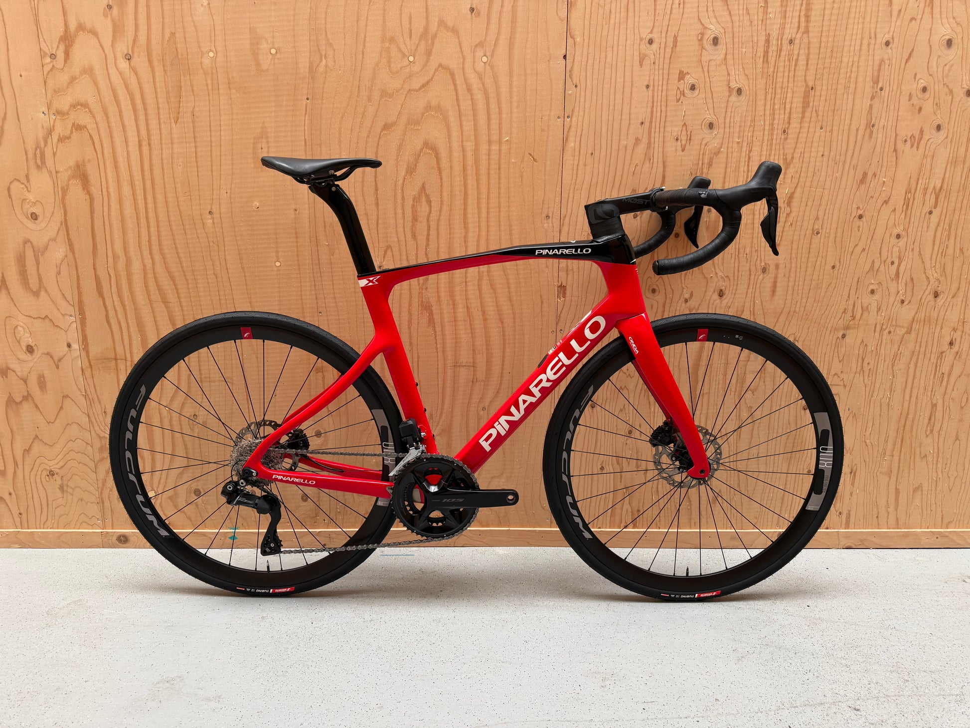 Zwarte Pinarello X3 racefiets met aerodynamisch frame en dunne banden, geplaatst op een weg.