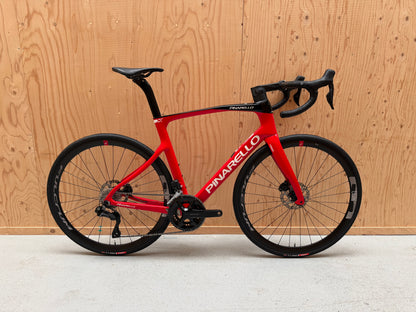 Zwarte Pinarello X3 racefiets met aerodynamisch frame en dunne banden, geplaatst op een weg.