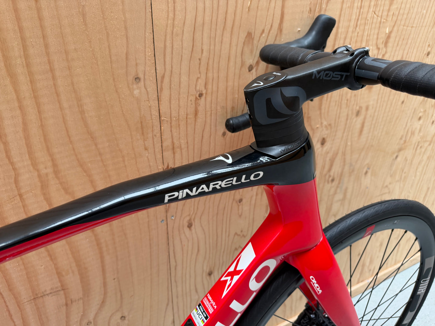 Zwart Pinarello X3 racefiets met aerodynamisch frame en dunne banden, geplaatst op een weg met groene achtergrond.