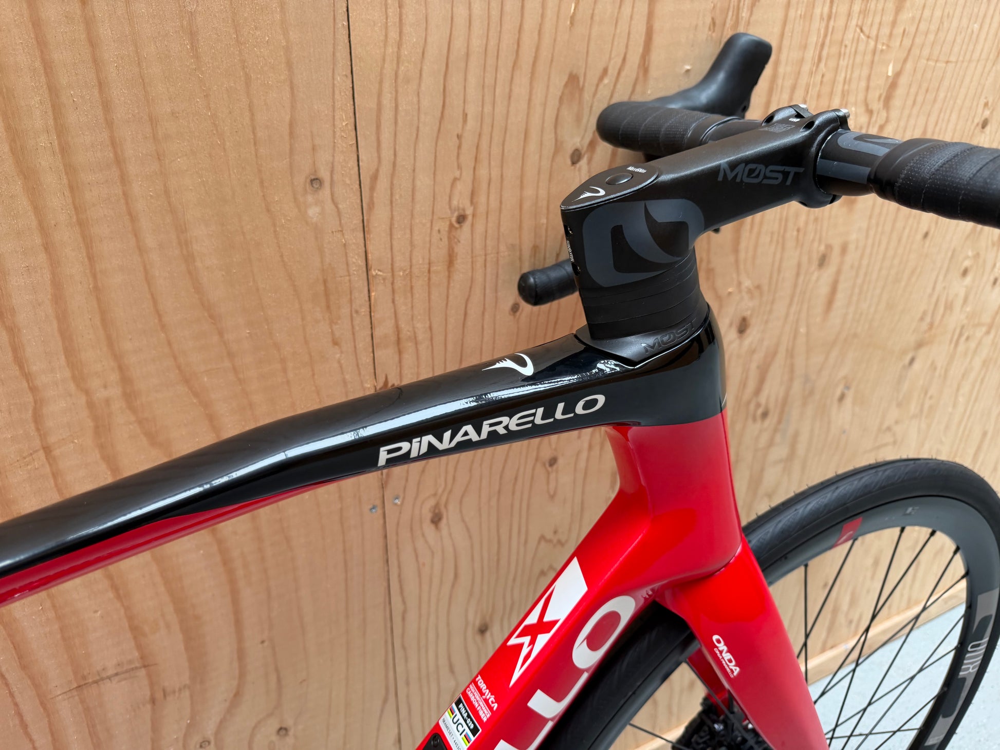 Zwart Pinarello X3 racefiets met aerodynamisch frame en dunne banden, geplaatst op een weg met groene achtergrond.
