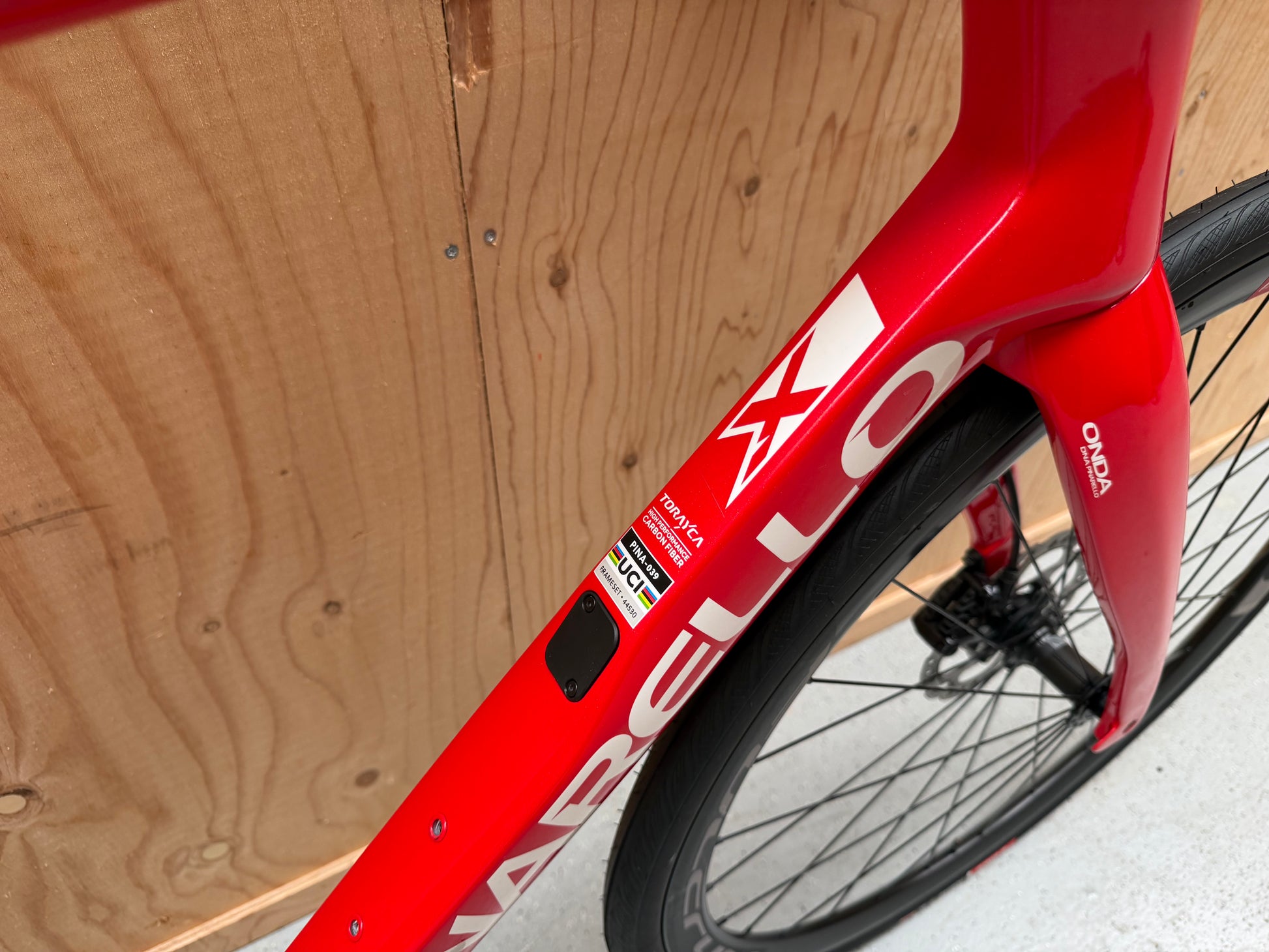 Zwarte Pinarello X3 racefiets met aerodynamisch frame en kniebeschermers, liggend op een witte achtergrond.