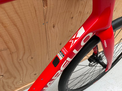 Zwarte Pinarello X3 racefiets met aerodynamisch frame en kniebeschermers, liggend op een witte achtergrond.